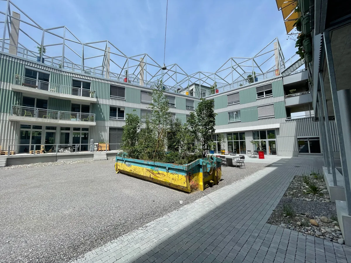 Auch dieser soll noch von den Bewohnern gestaltet werden.  Bild von einem Innenhof mit Pflanzen in Baugruben und viel Beton und Kies.